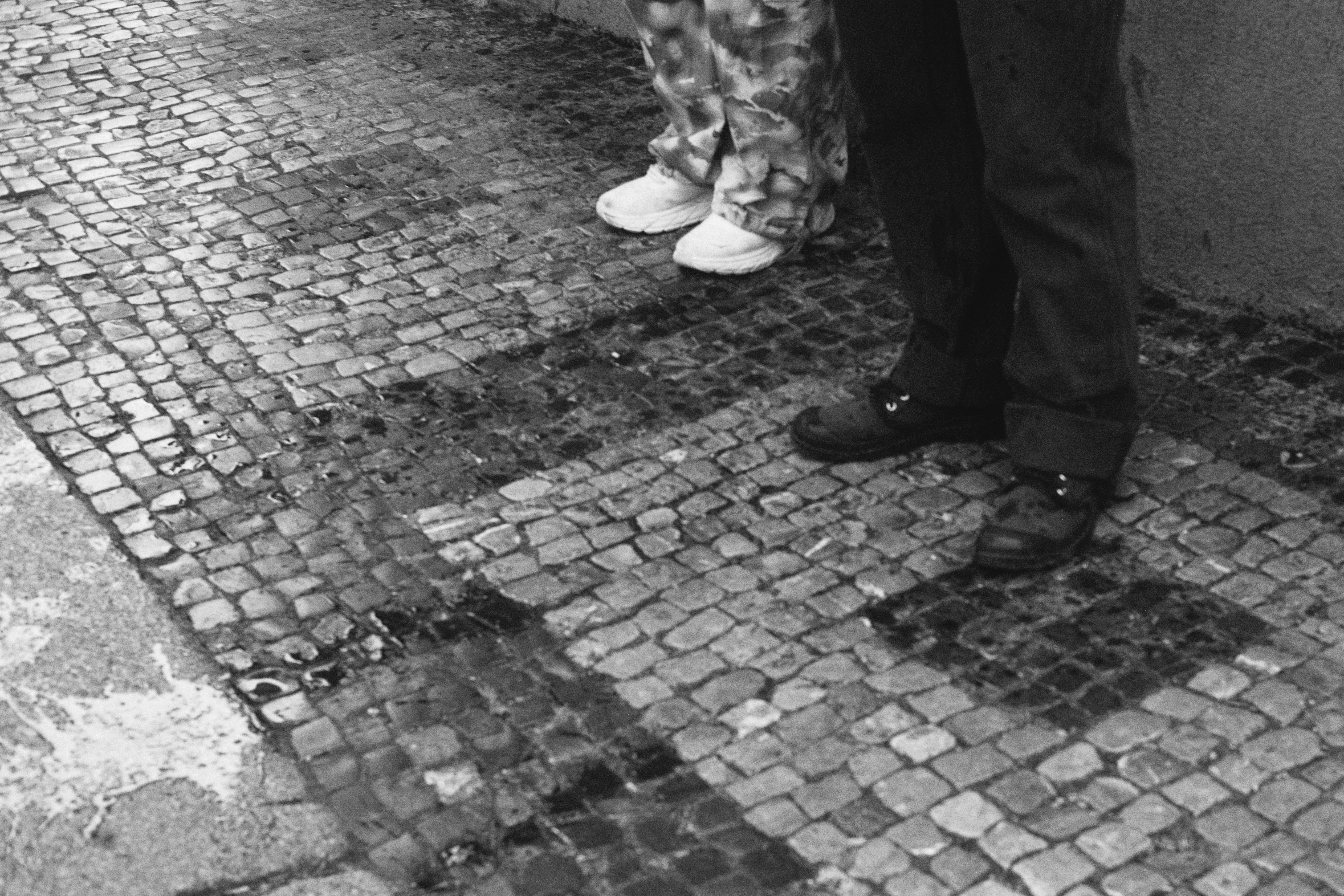 a black and white photograph of water on the ground next to partcipant's shoes