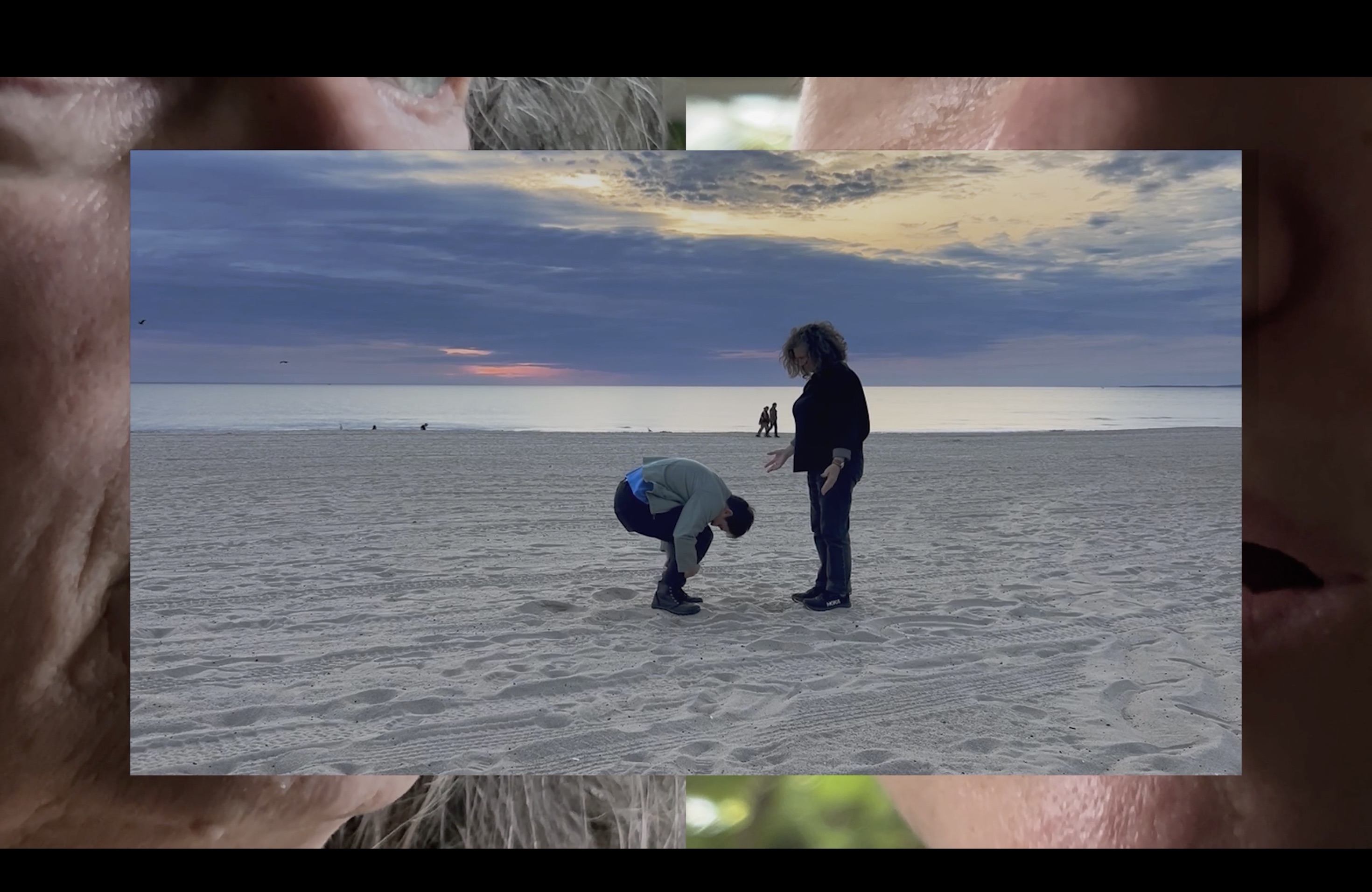 a still of a film. two peoples faces frame an inner image of one person crouching on a beach while another looks on