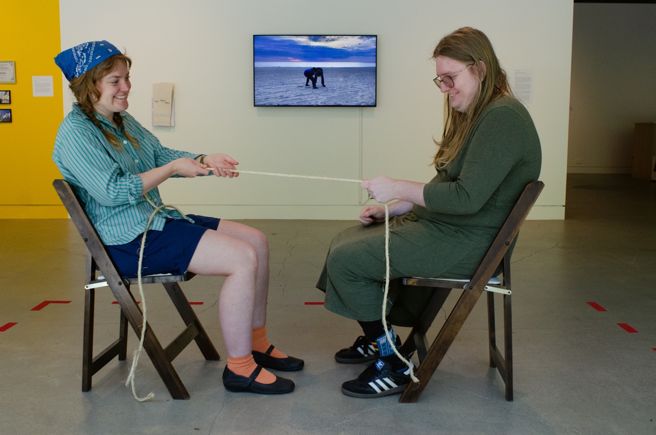two white blond people smiling tug on a rope while sitting in chairs