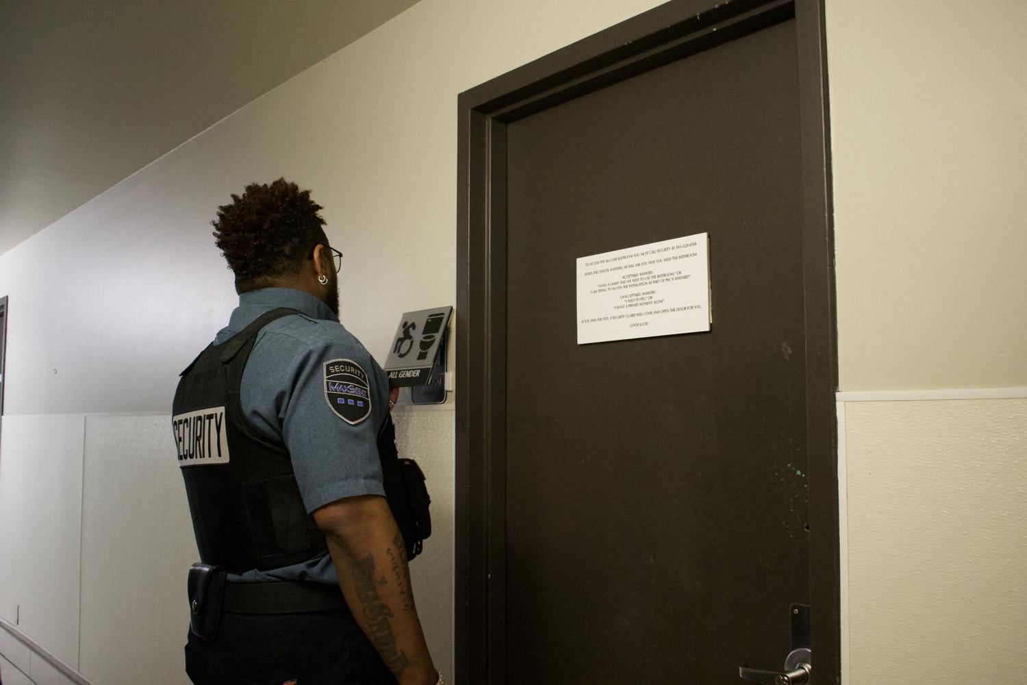 a security guard removes the all-gender restroom sign outside of the bathroom